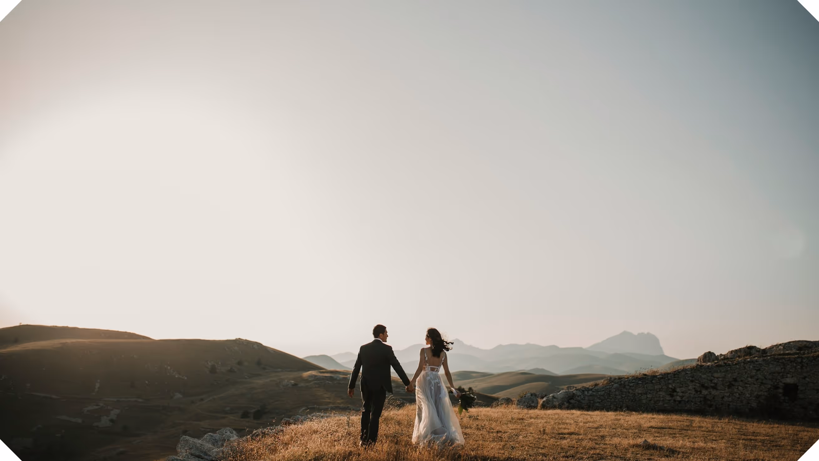 a man and woman holding hands in a field with hills in the background