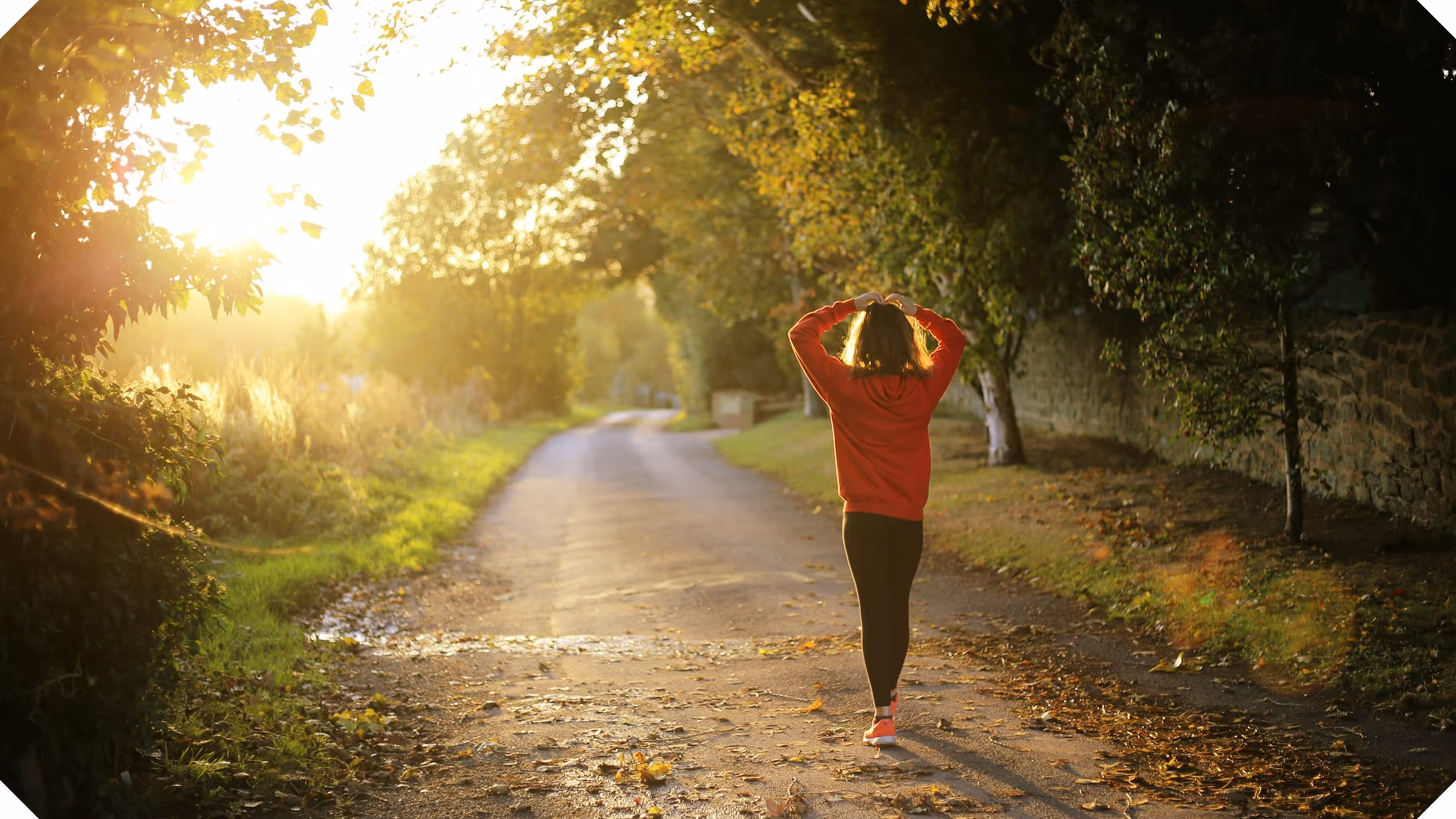 a woman walking on a road with trees and a sunset