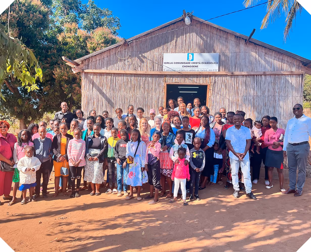 Two missionaries standing with dozens of local people in front of a church in Mozambique