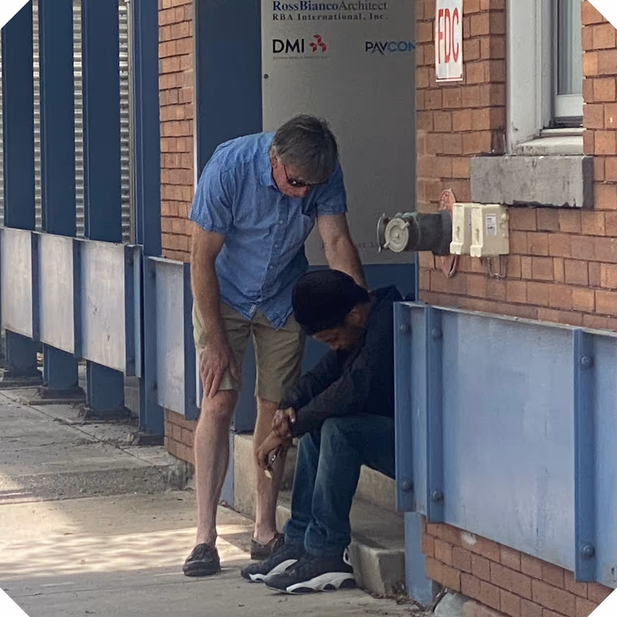 a man sitting on a ledge outside a building while another man prays for him