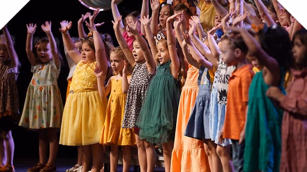 a group of children raising their hands from stage while performing a song