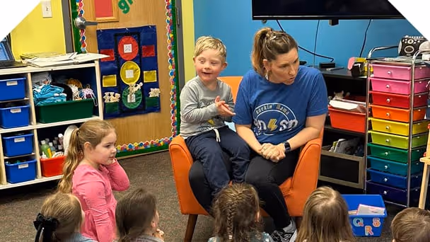 a teacher and preschooler sitting in front of the class