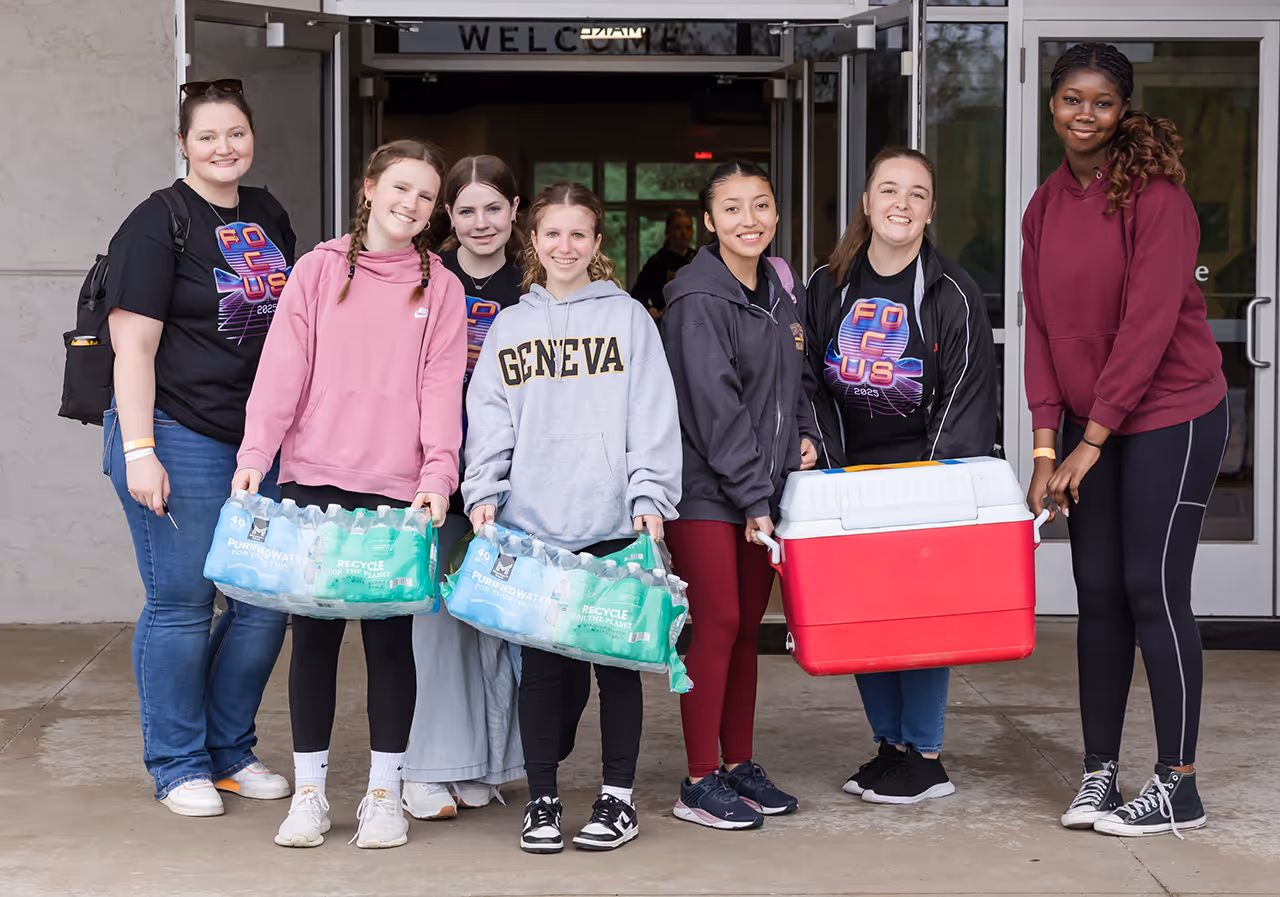 A group of students posing together with bottled water and supplies for a service project