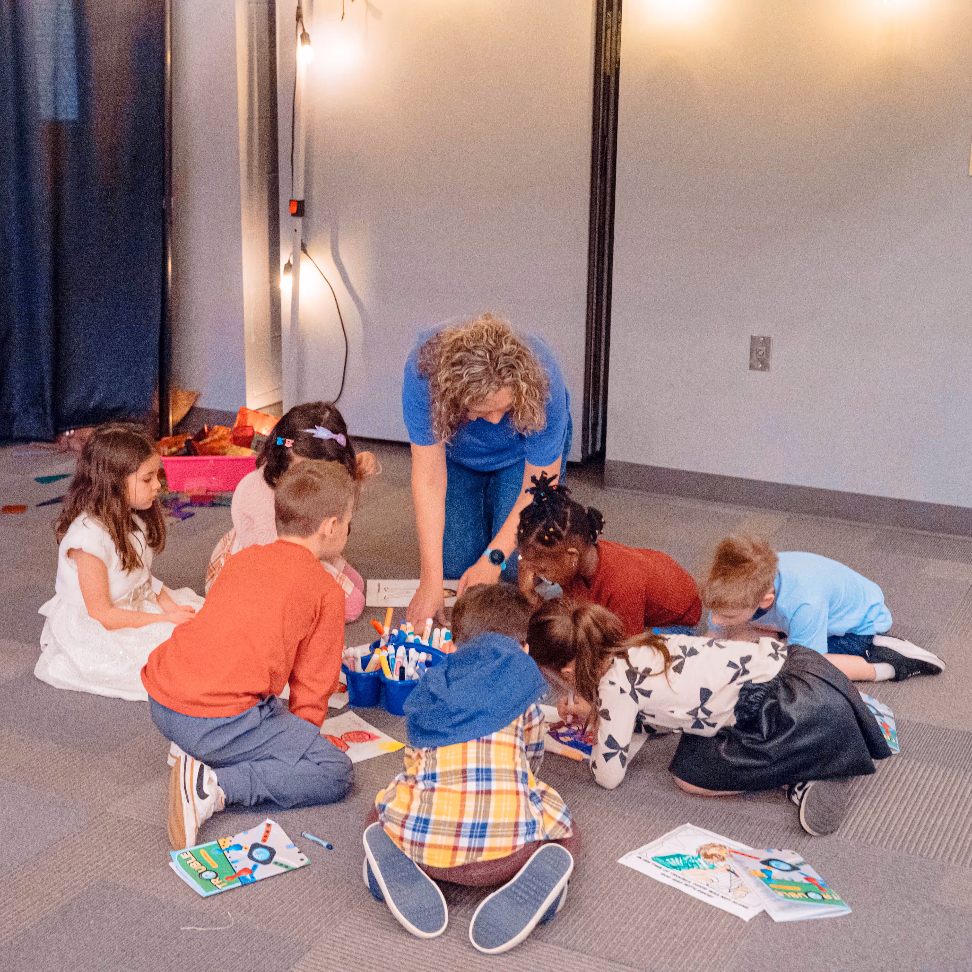 Seven children sitting together for small group time, along with their adult leader