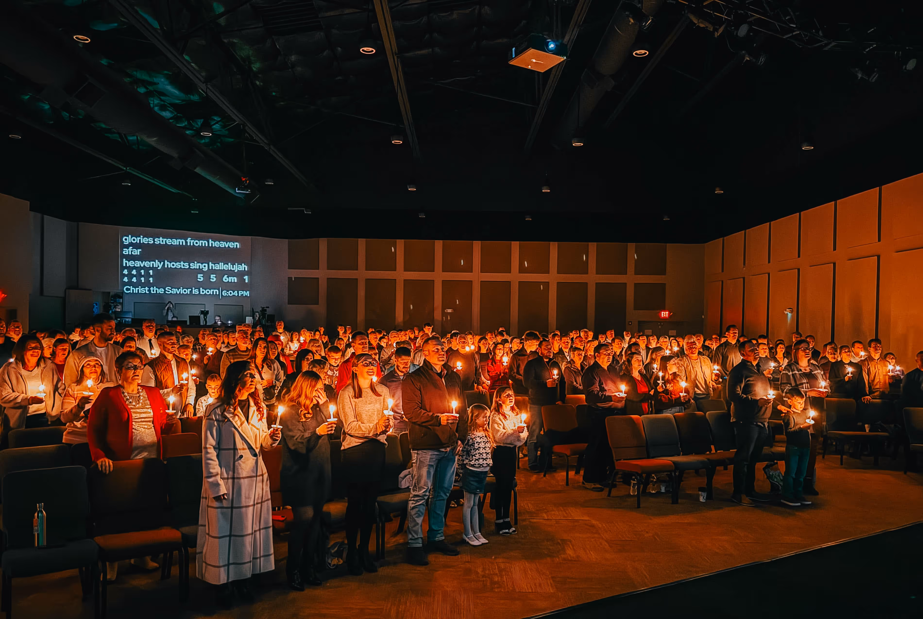 Large group of people holding lit candles inside a dimly lit church during a candlelight service.