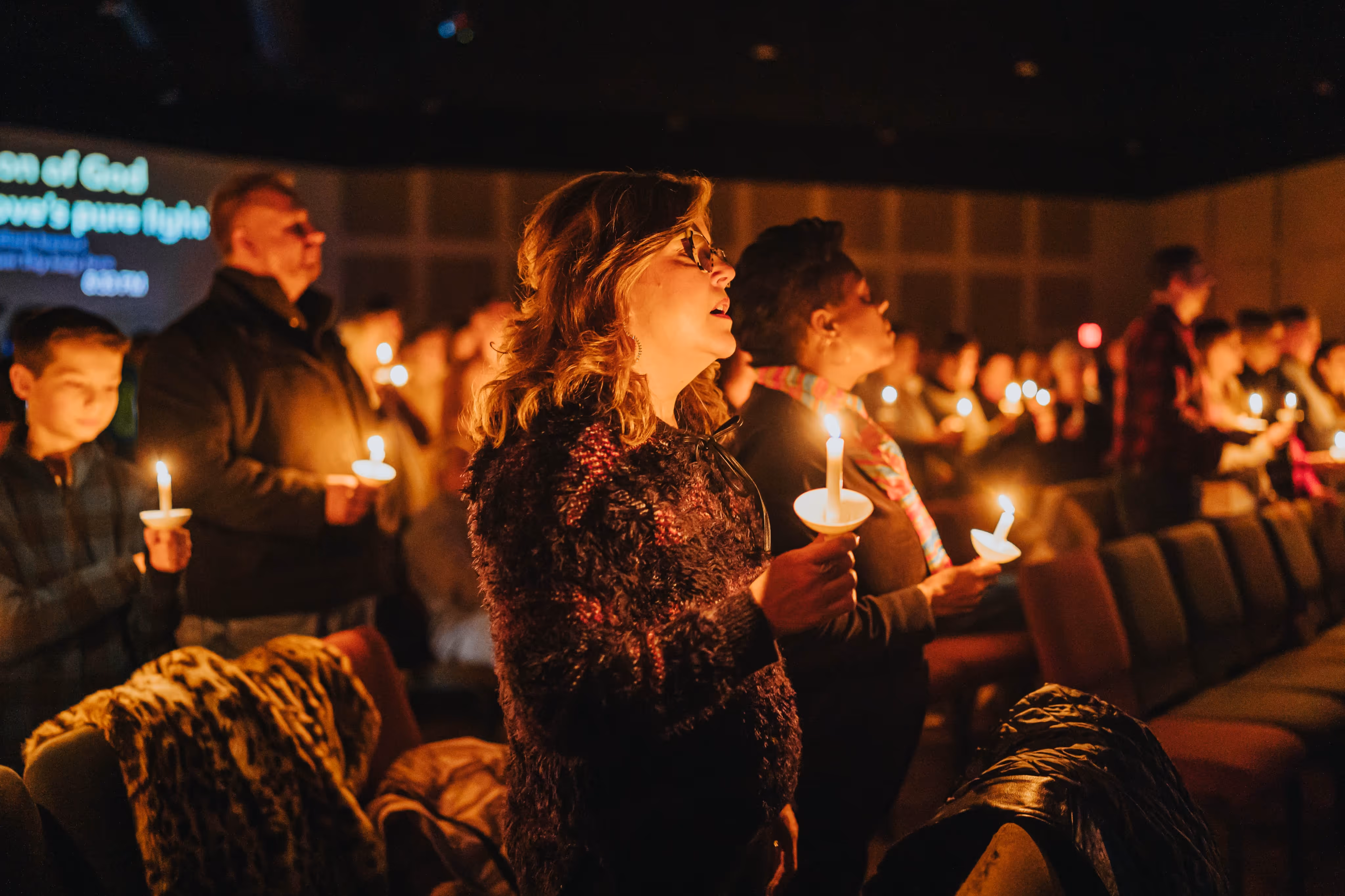 Group of people standing indoors holding lit candles during a candlelight service.