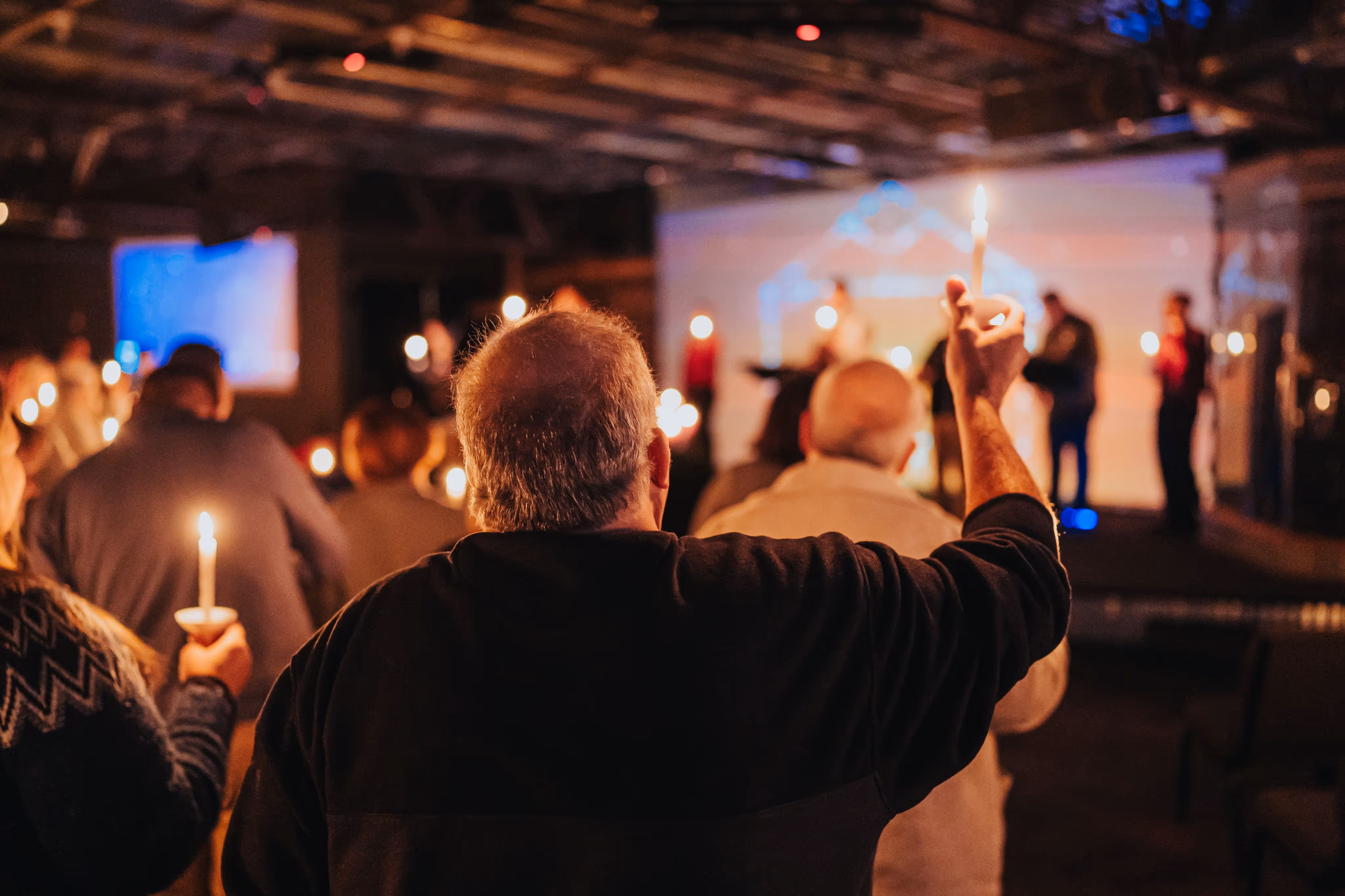People gathered indoors holding lit candles during a candlelight vigil or ceremony.