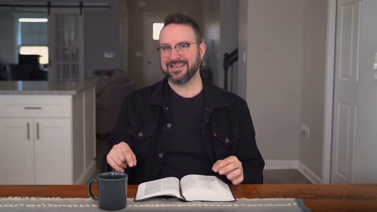 a man sitting at a table with a book and a mug