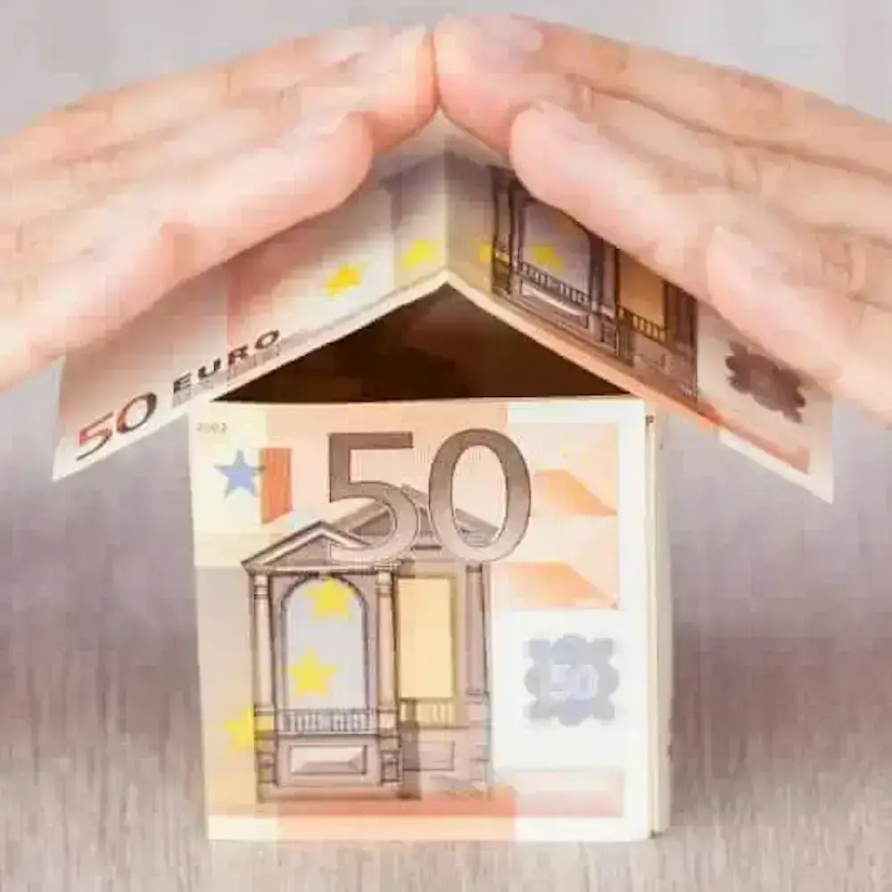 Billets de 50 euros pliés en forme de maison protégés par des mains