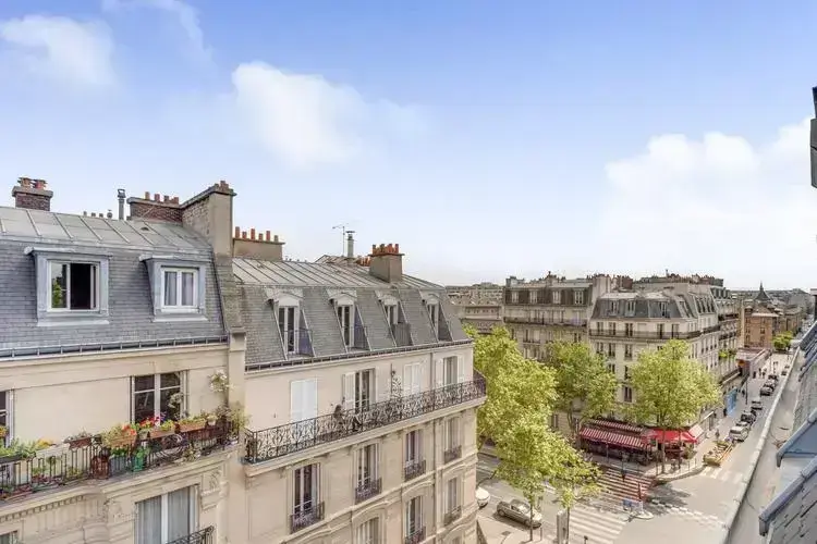 Vue sur des immeubles haussmanniens typiques à Paris avec des balcons en fer forgé et des toits mansardés, mettant en valeur l’héritage architectural du Baron Haussmann.