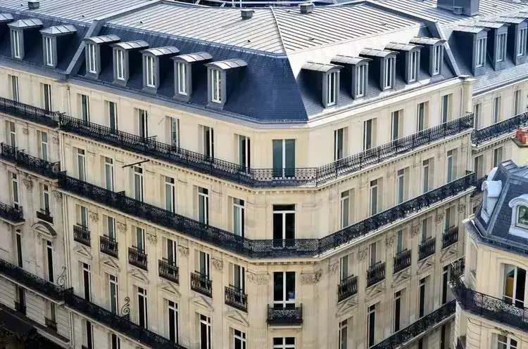 Façade élégante d'un immeuble parisien, avec balcons en fer forgé et toits mansardés.