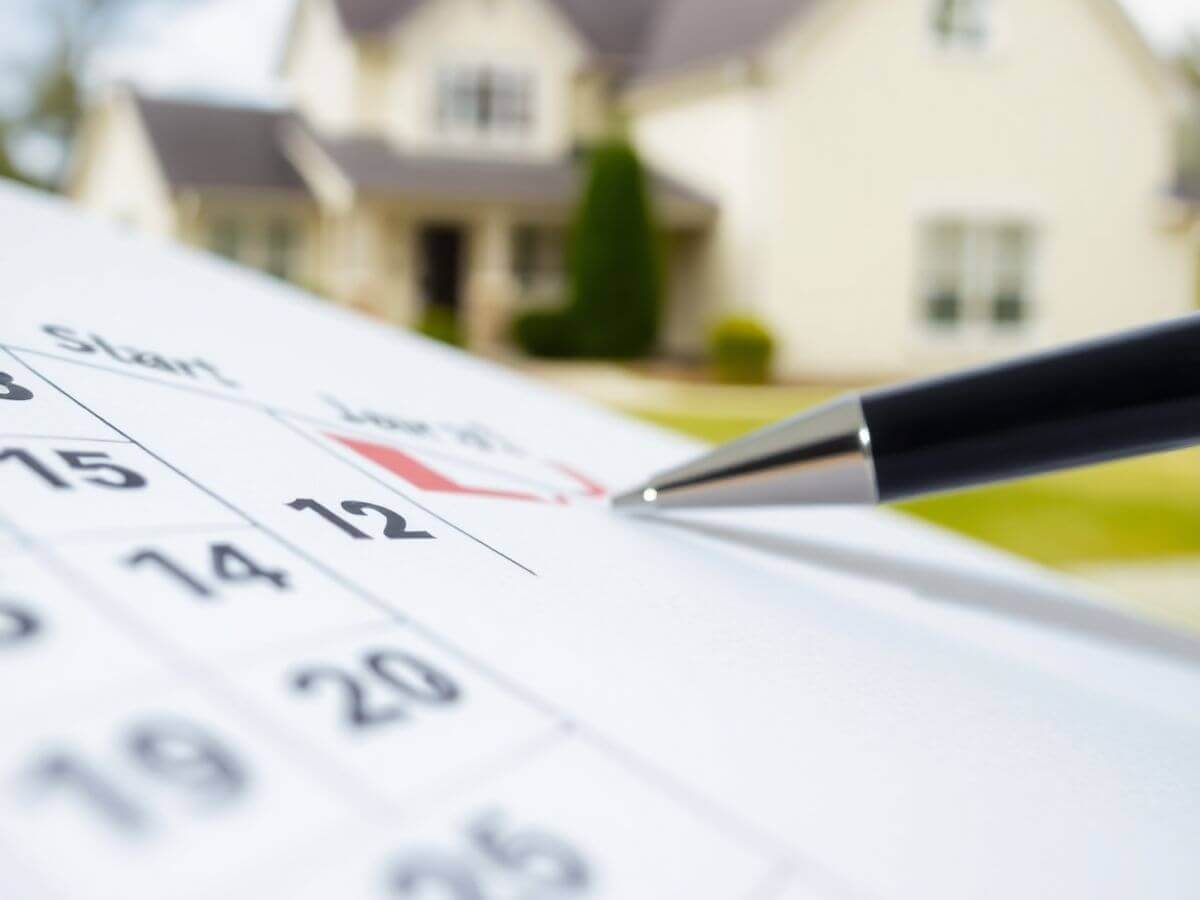 Calendrier avec dates marquées et une maison floue en arrière-plan.