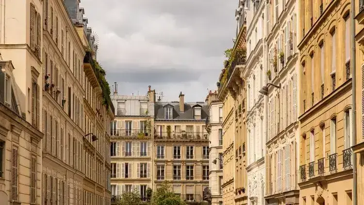 Rue pittoresque à Paris, entourée d'immeubles haussmanniens aux façades colorées et balcons fleuris.