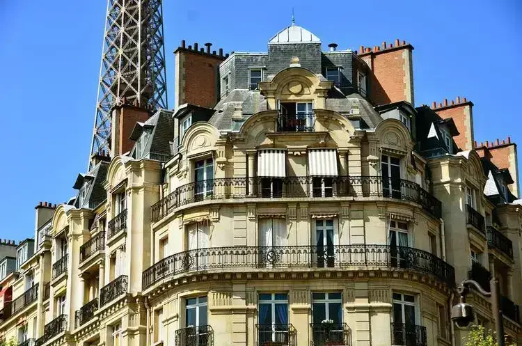 Façade d'un immeuble haussmannien typique à Paris avec vue sur la Tour Eiffel, illustrant l'élégance architecturale et l'urbanisme du Grand Paris.