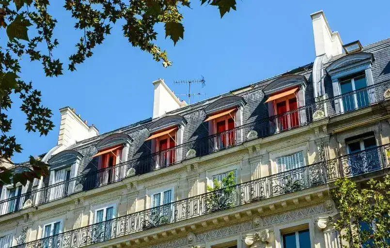 Façade d'un appartement traditionnel à Paris, mettant en valeur de charmantes fenêtres avec balcons et un toit en ardoise.