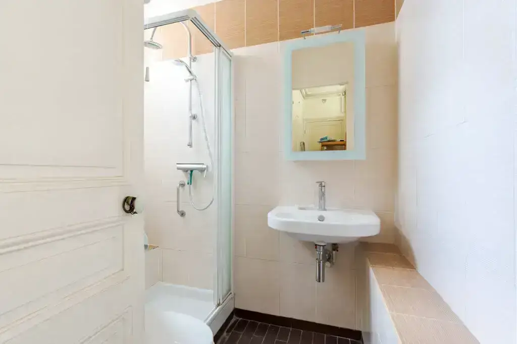 Clean, compact bathroom with glass shower, white sink, and blue-framed mirror