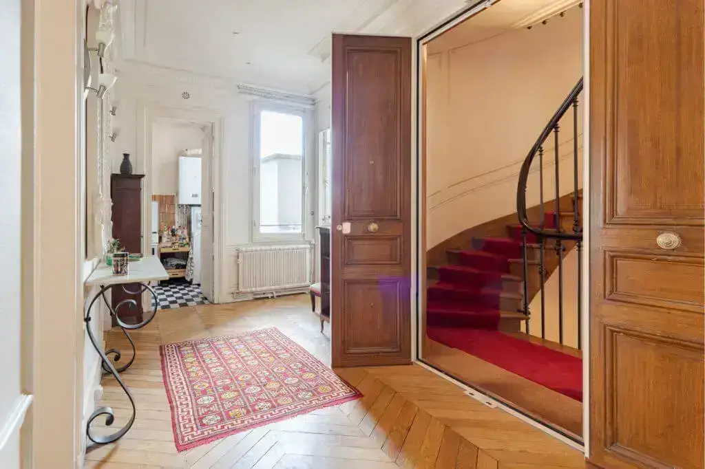Elegant entryway with wooden floors, red carpet stairs, and decorative rug