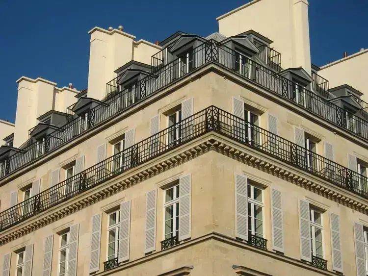 Façade élégante d'un immeuble haussmannien à Paris, avec balcons en fer forgé et fenêtres lumineuses.