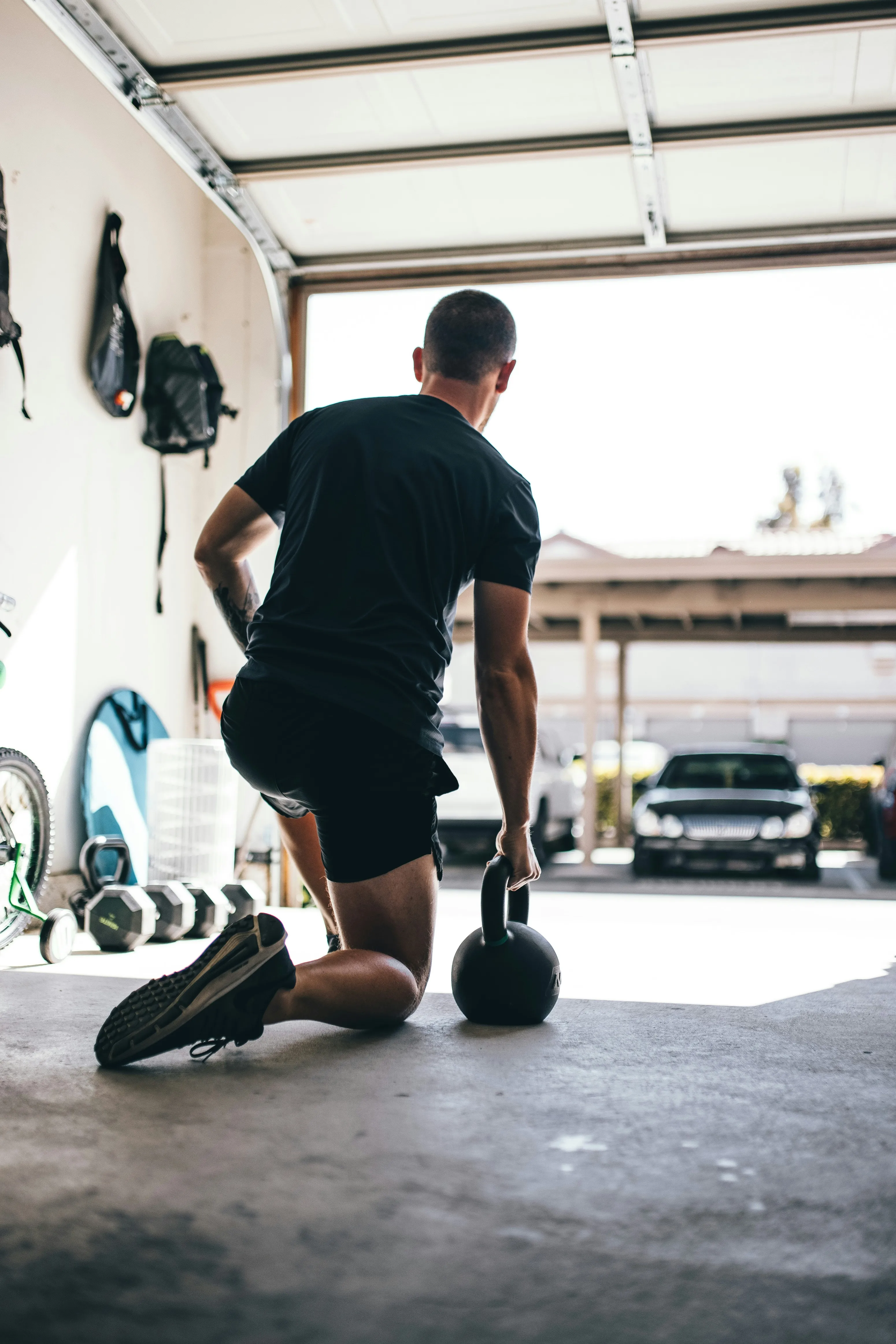 Man exercising with a kettlebell on one knee inside a garage gym.