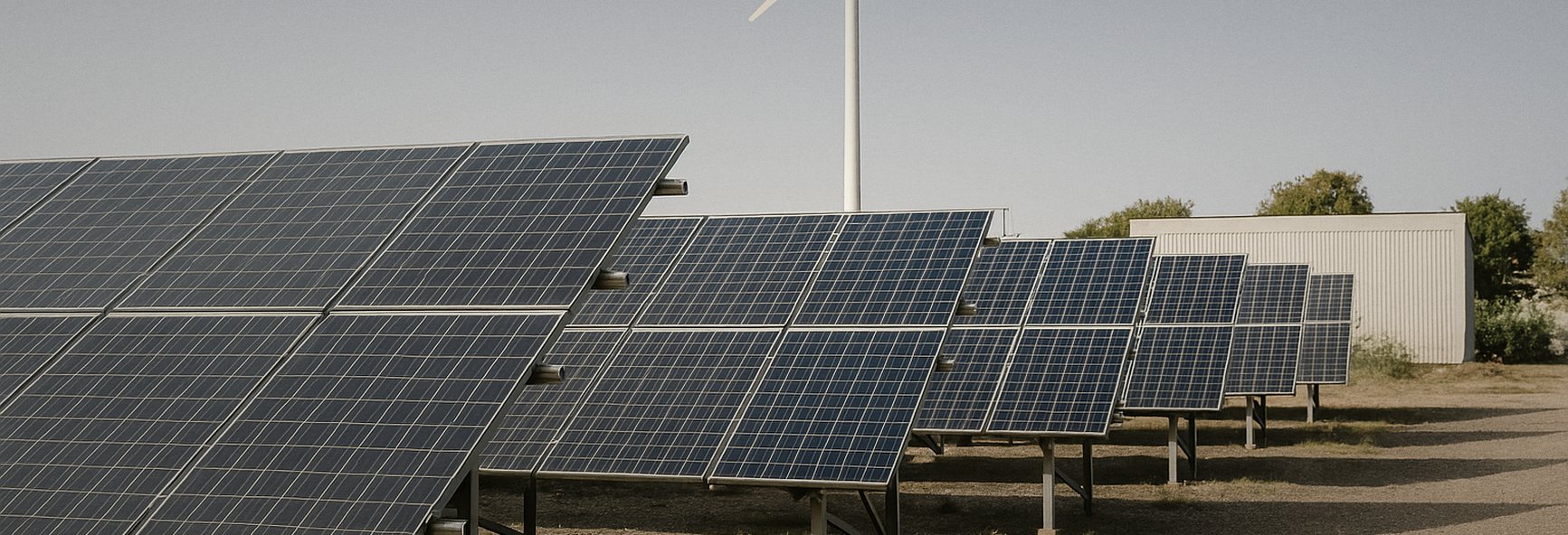 rows of solar panels and a small wind turbine at a clean energy test site under a clear sky