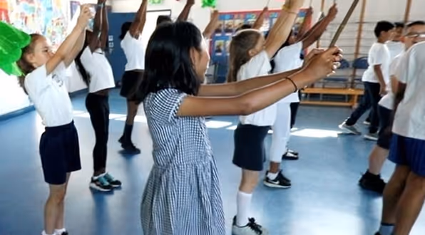 School children dancing in unison during a fun and interactive workshop led by a professional instructor.

