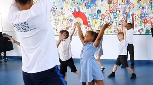 Excited kids expressing creativity through movement in a classroom-based dance workshop setting.

