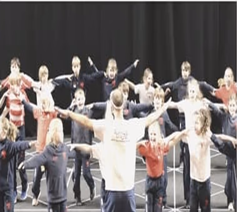 Group of school children joyfully dancing during a workshop activity, showcasing energy and participation.