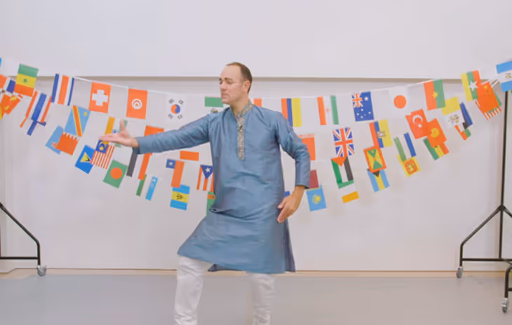 Instructor leading a vibrant Indian dance workshop, showcasing expressive hand gestures and energetic moves in a school setting.

