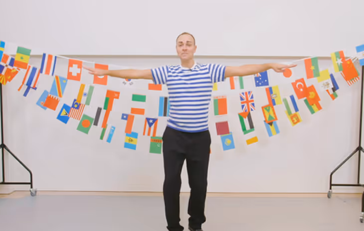 Instructor demonstrating traditional Greek dance steps during a school workshop, engaging students with cultural music and group movements.

