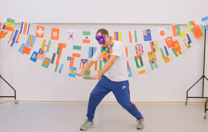 Instructor leading a lively carnival dance workshop, demonstrating samba-inspired moves in a school setting with international flags decorations in the background.

