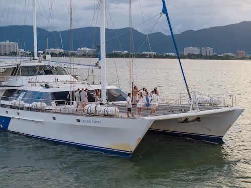 Group of people standing and socialising on the deck of Ocean Spirit, with buildings and mountains in the background.