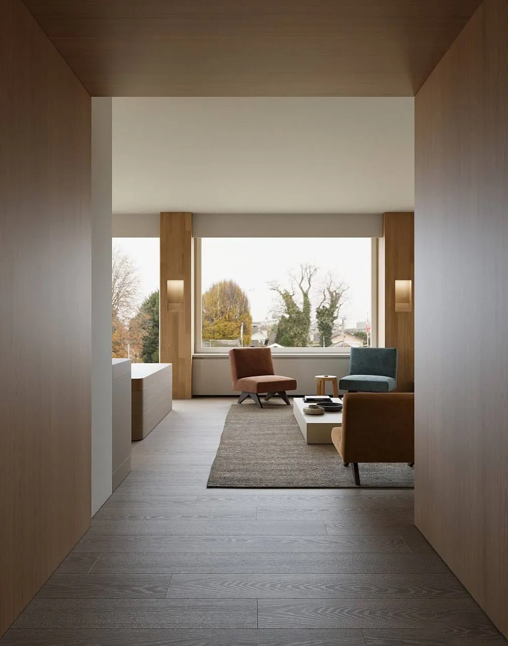 Minimalist living room with gray wood flooring, large window, three modern chairs in brown and blue, a low white coffee table on a gray rug, and warm wooden wall accents.