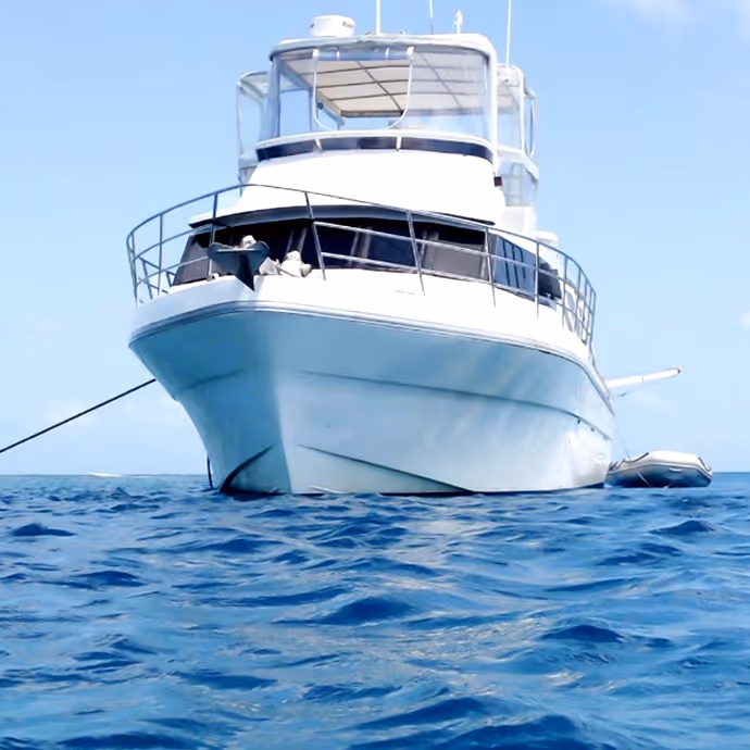 Front view of a luxurious white yacht anchored on calm blue ocean waters under a clear sky.