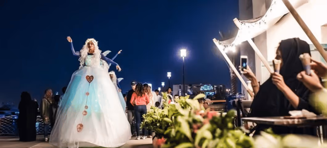 Performer dressed in an elaborate, fairy-tale-inspired gown entertaining a crowd at night during a street event or festival.