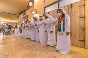 Group of men in traditional Emirati attire performing a cultural dance inside a heritage-style marketplace.