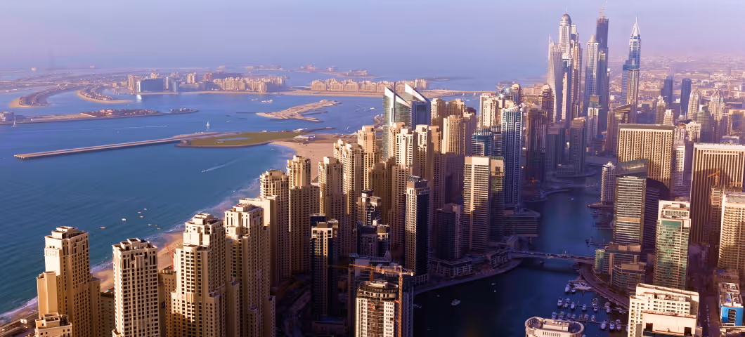 Aerial view of Dubai Marina with towering skyscrapers, winding waterways, and the Palm Jumeirah visible in the distance.
