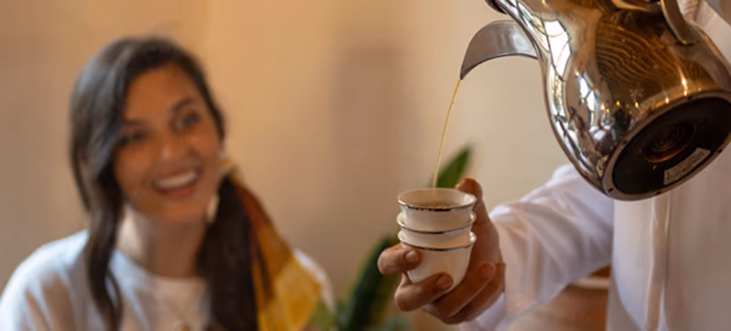 Smiling woman being served traditional Arabic coffee from a dallah pot into a small cup.