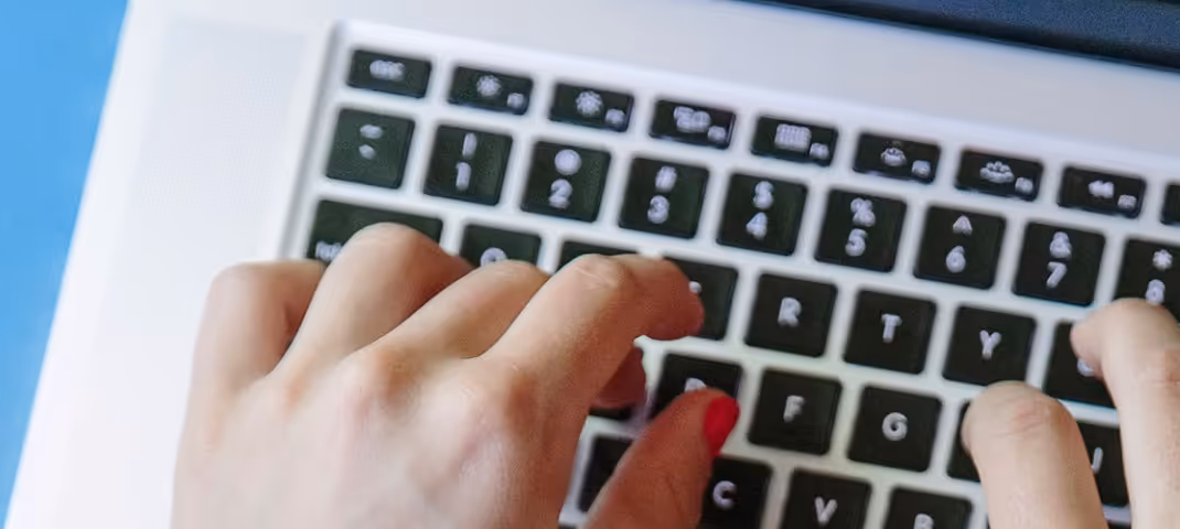 Close-up of a person typing on a laptop keyboard with both hands.