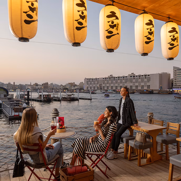 People sitting at an outdoor waterfront café decorated with Japanese lanterns during sunset.