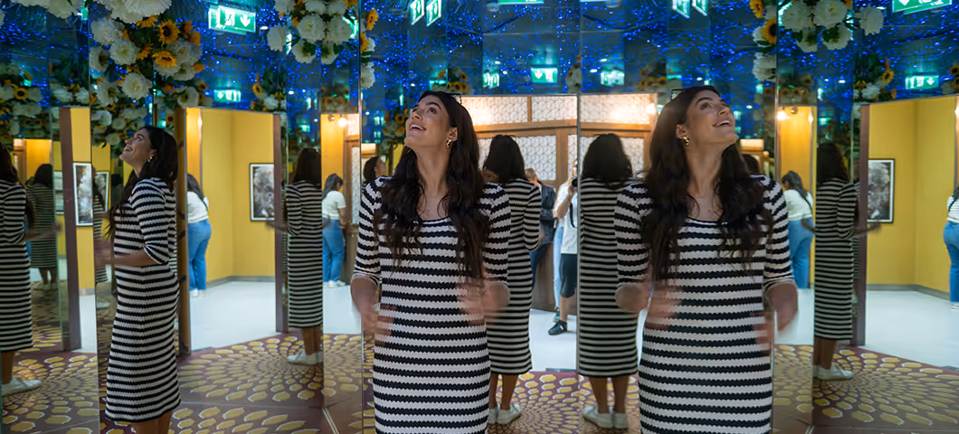 Woman walking through a mirrored hallway with reflections creating multiple images.