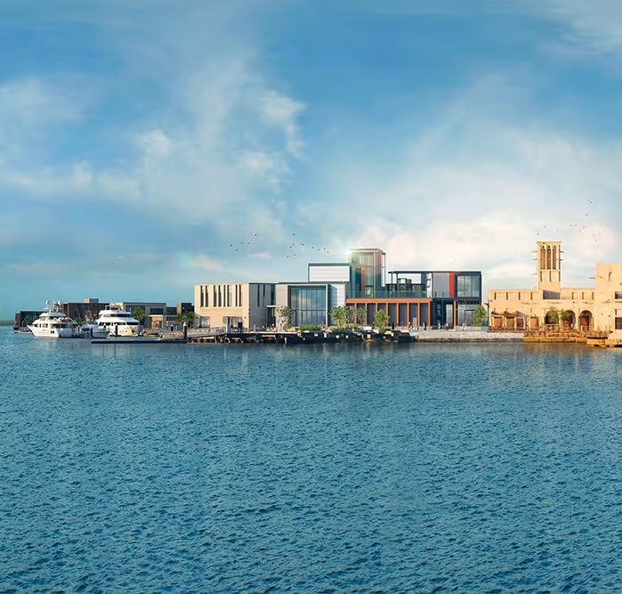 Scenic waterfront view showcasing yachts docked beside a mix of modern glass buildings and traditional Emirati wind tower architecture at Al Seef, Dubai.