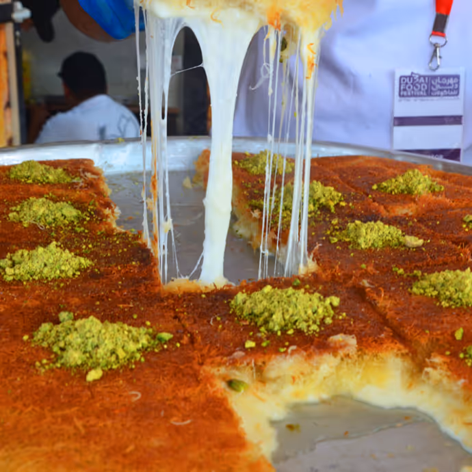 Freshly prepared cheese kunafa being served, with melted cheese stretching and topped with ground pistachios.