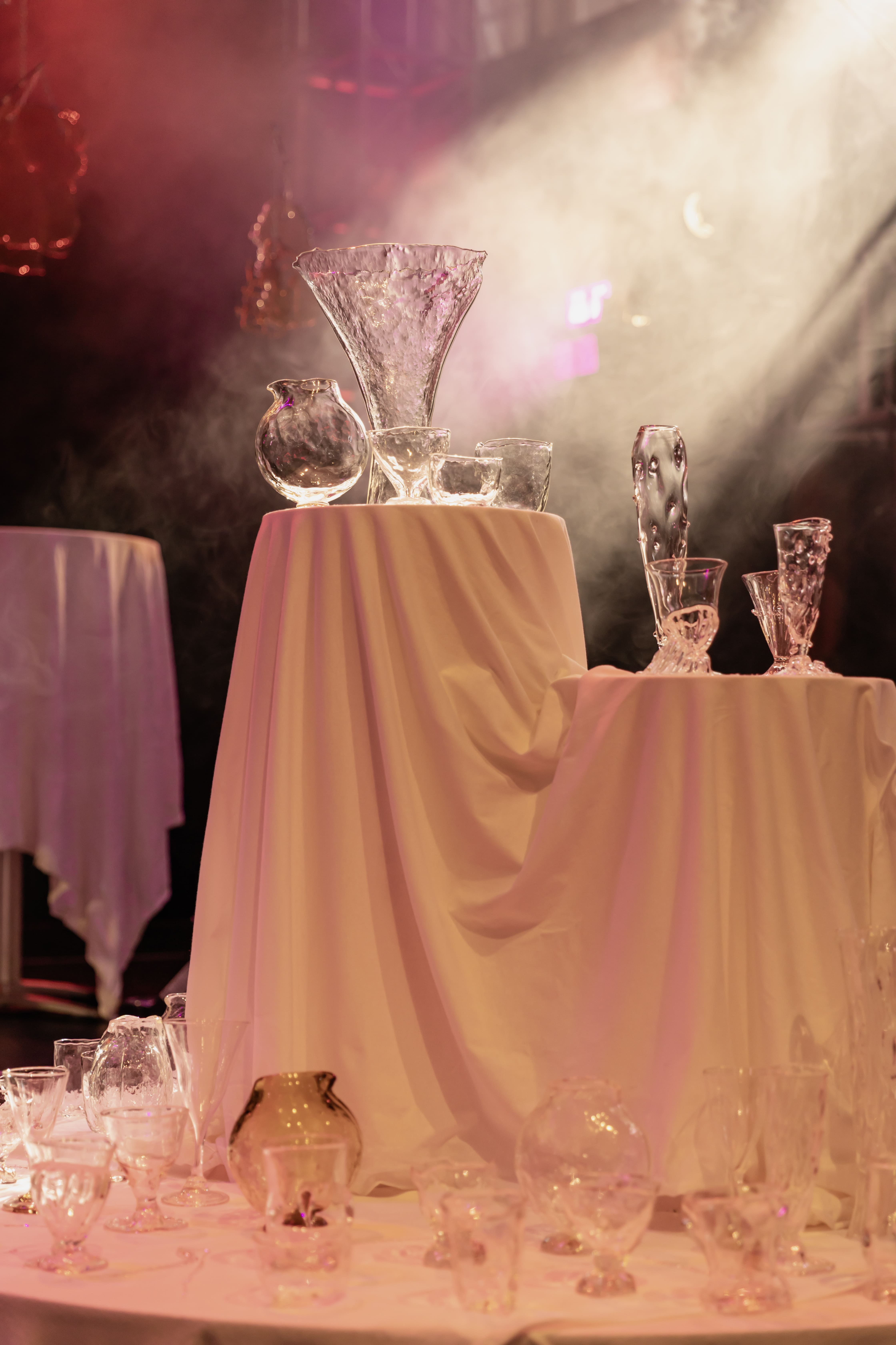 Image of clear glass vessels on a structure covered in draped white fabric with dramatic lighting 
