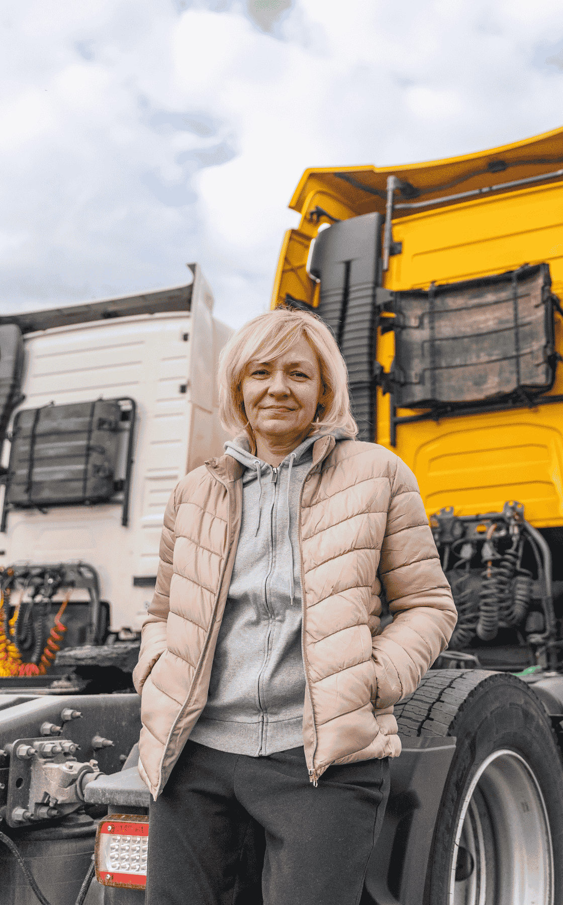 Lady Trucker standing behind her truck, It's a yellow semi truck without a trailer.