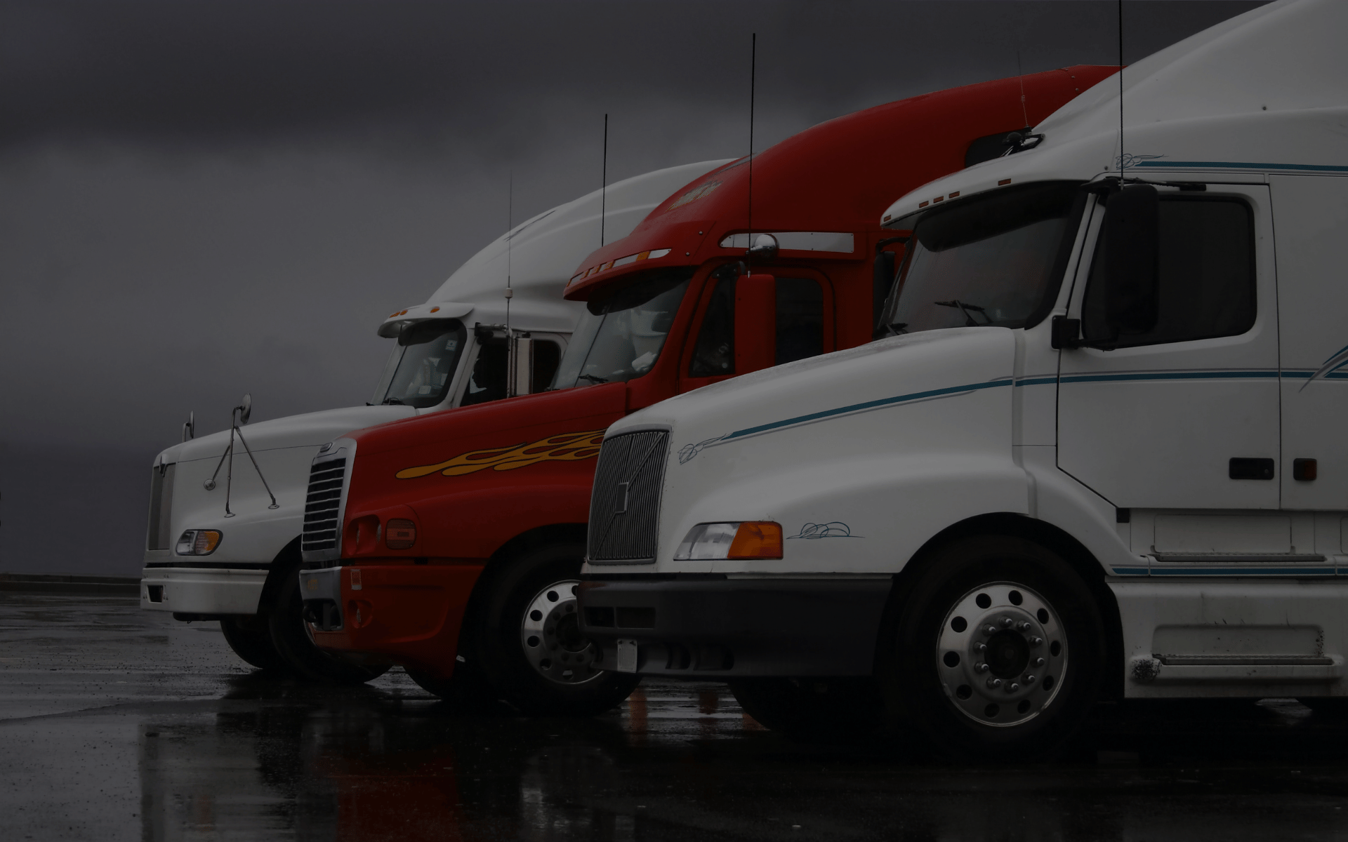 Three trucks parked on a wet road, and there are dark rain clouds in the background.