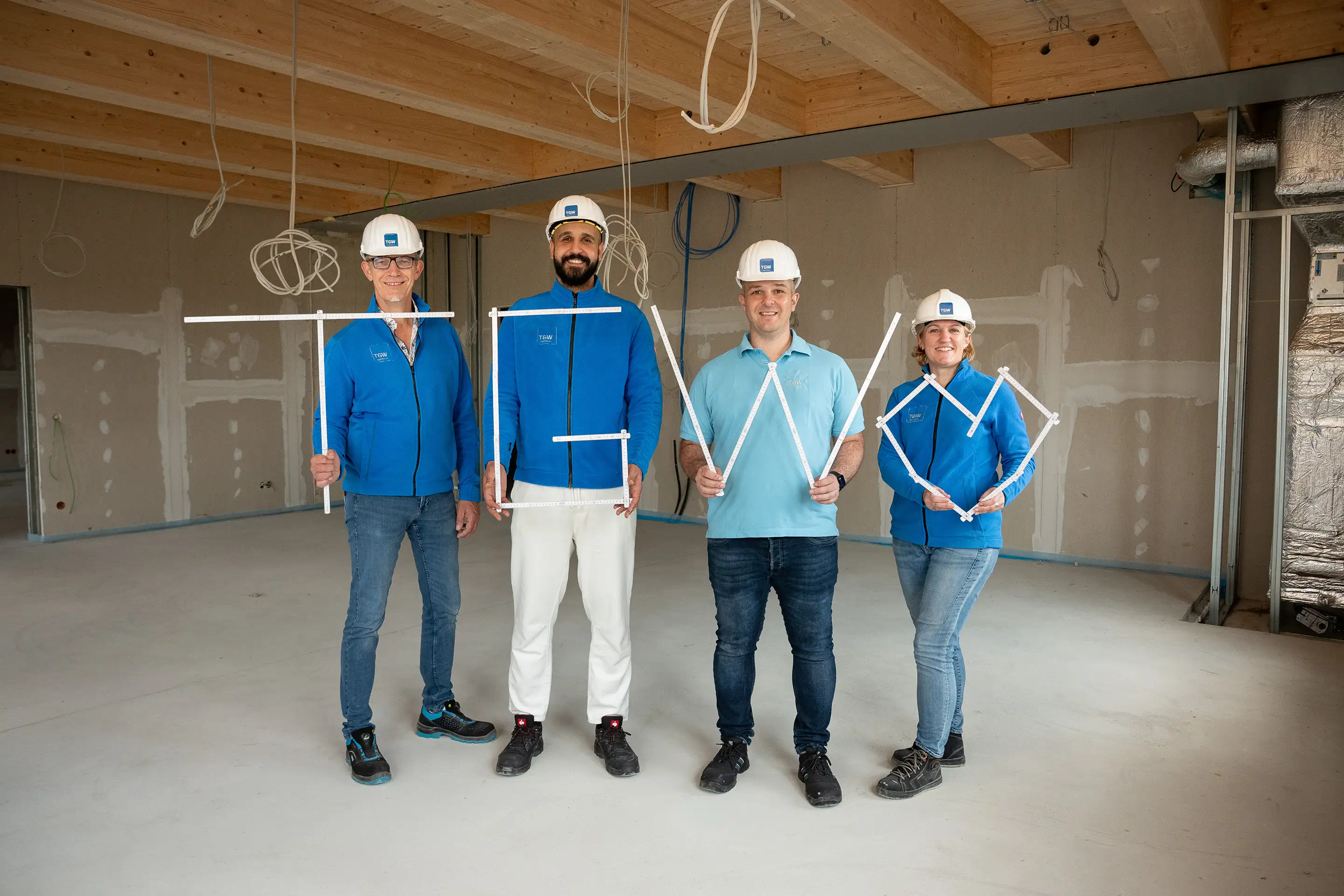 TGW Planung | Mitarbeiterinnen und Mitarbeiter zeigen mit Zollstöcken TGW und Herz