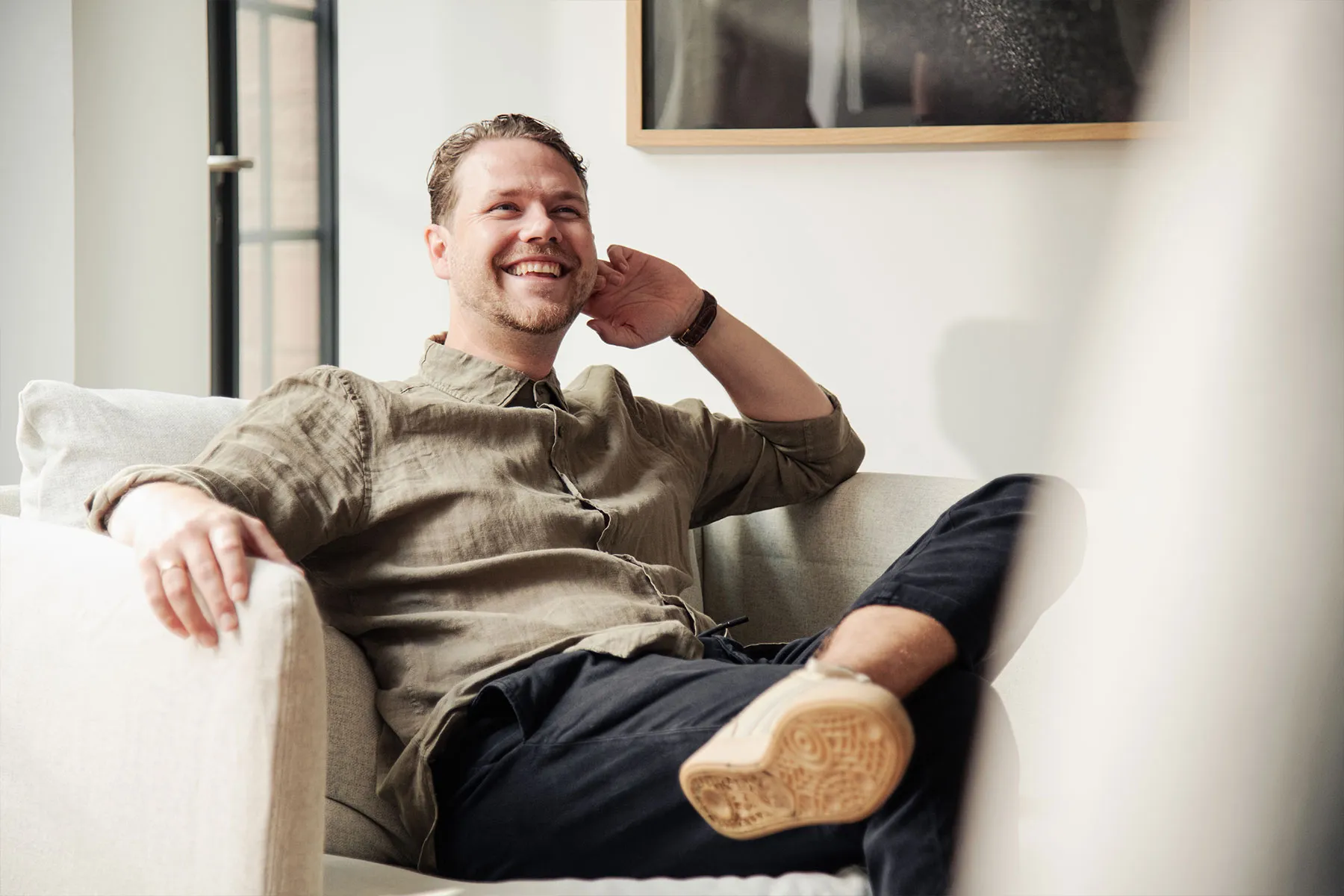 Ein Mitarbeiter sitzt auf der Couch und lacht.