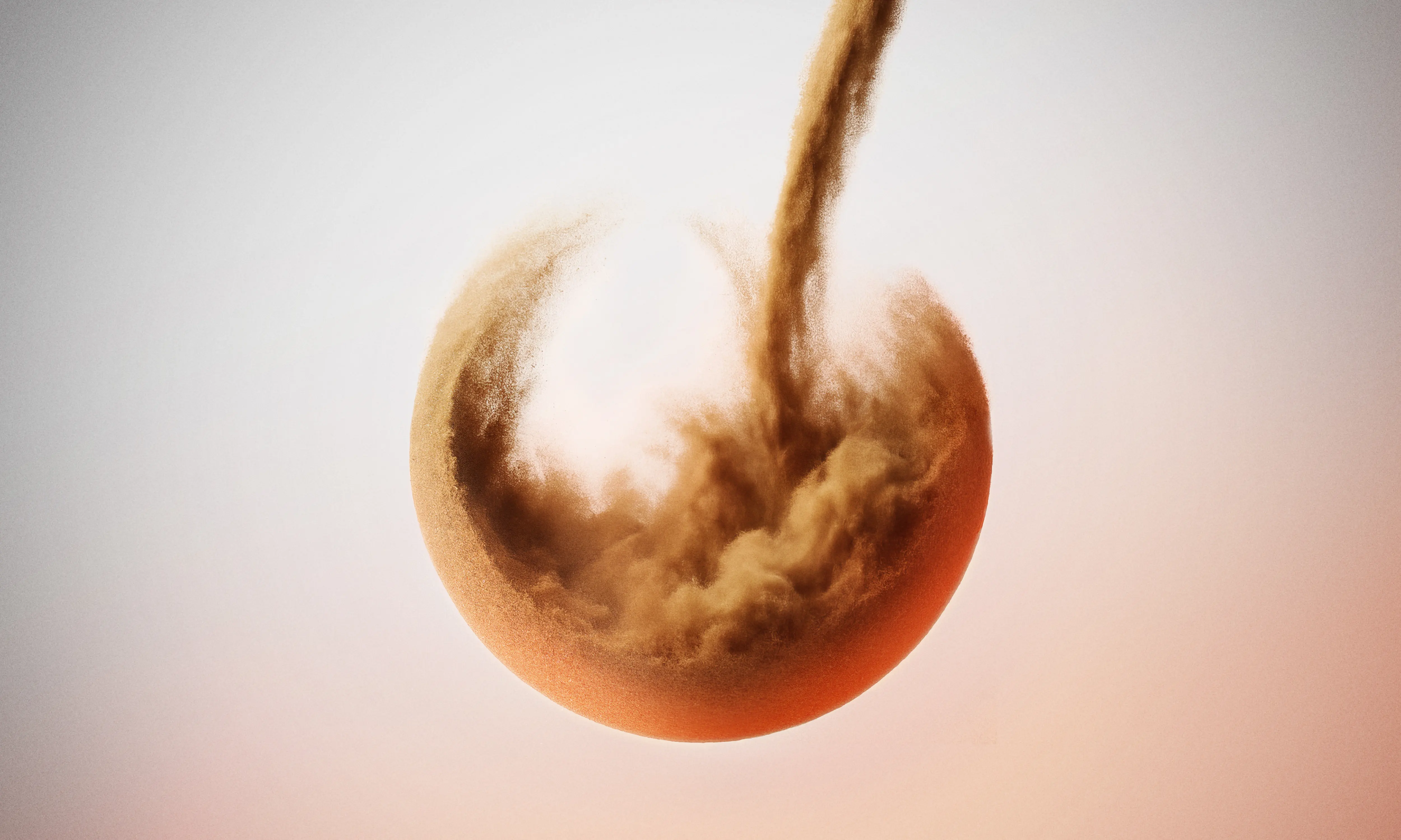 Brown powder forming a sphere as more powder flows into it against a light gradient background.