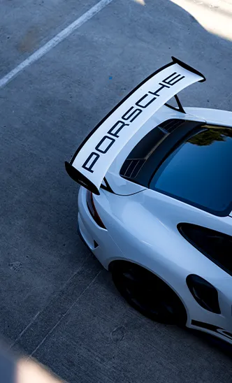 Detailaufnahme des markanten Heckflügels mit PORSCHE Schriftzug auf einem weißen Sportwagen des ESC European Speed Club.

