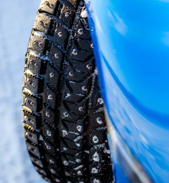 Detailaufnahme eines Spikereifens an einem blauen Sportwagen für das ESC Icedriving-Event in Schweden.

